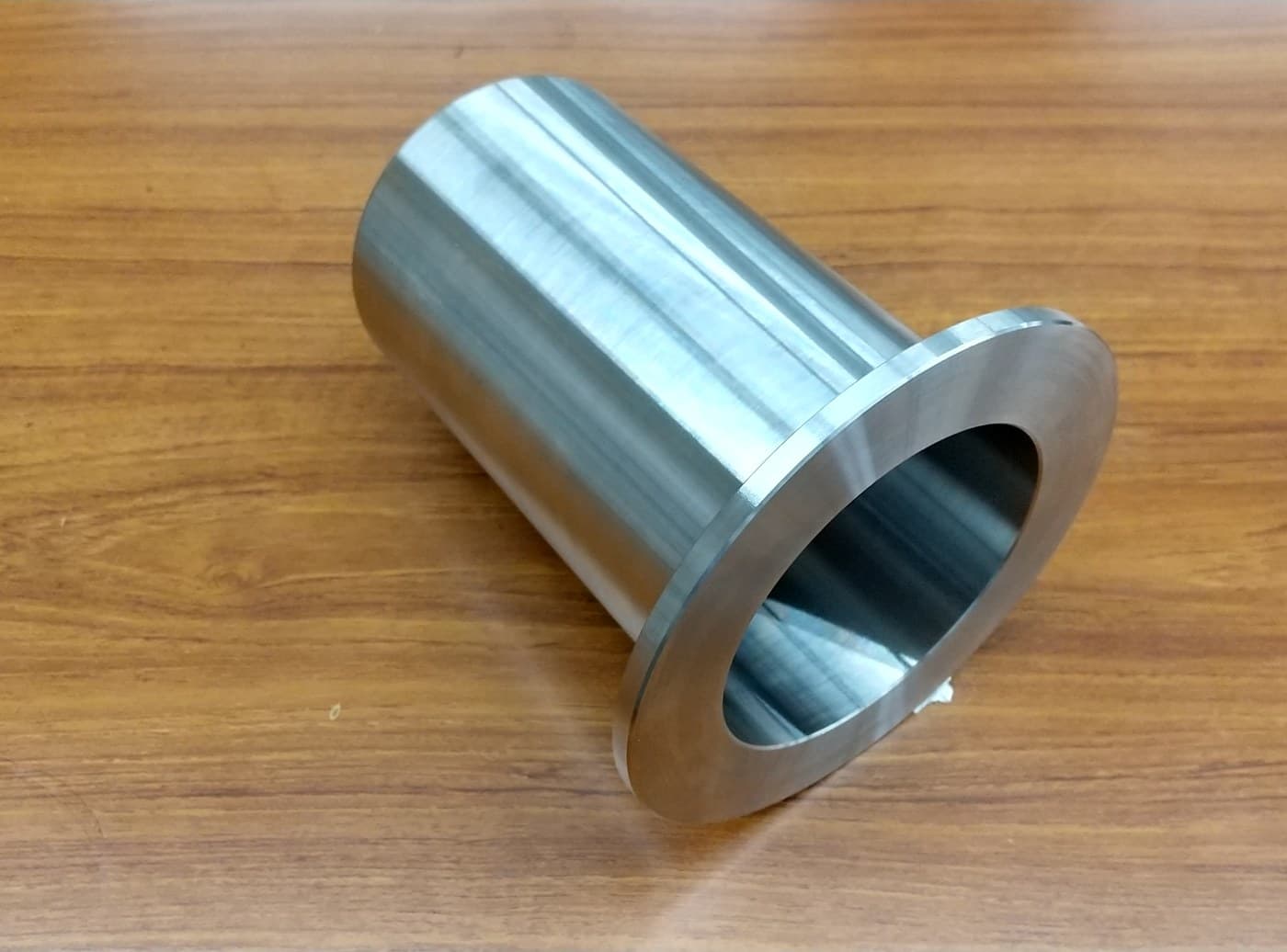 木目の机に置かれた、片側の端に円形のつばがある金属製の筒状部品。内径の仕上げ面が見える